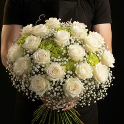 Bouquet "Majesté de Givre" ​L'Esprit de la Création ​Une composition majestueuse qui incarne la pureté et le raffinement. Ce bouquet rond et dense joue sur l'harmonie parfaite du blanc et du vert tendre pour un rendu à la fois chic et apaisant. C'est le choix d'excellence pour célébrer un mariage, une cérémonie, ou pour offrir un cadeau de prestige qui illuminera tout intérieur avec une élégance intemporelle. ​Détails de la Composition ​Chaque bouquet est confectionné avec une exigence de qualité absolue par nos artisans : ​Fleurs Nobles : Une profusion de roses blanches à gros boutons, symboles de pureté et d'élégance. ​Cœur de Bouquet : Des œillets d'un vert pomme vibrant qui apportent une structure moderne et une texture veloutée. ​Finition Vaporeuse : Un nuage de gypsophile blanc vient envelopper les fleurs, ajoutant une légèreté aérienne et une touche de délicatesse. ​Forme : Un travail de montage en bouquet rond serré pour une tenue parfaite et une présentation haut de gamme.