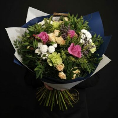 Bouquet "Jardin de Tendresse" ​L'Esprit de la Création ​Une composition généreuse et champêtre qui célèbre la douceur des nuances pastel. Ce bouquet se distingue par sa grande variété de fleurs, offrant un relief unique et une allure "fraîchement cueilli". Le mélange harmonieux de rose poudré, crème, blanc et vert tendre en fait le cadeau idéal pour exprimer son affection, fêter un anniversaire ou remercier avec élégance. ​Détails de la Composition ​Chaque création est une pièce unique assemblée avec soin dans nos ateliers de Roncq et Wervicq-Sud : ​Fleurs Majeures : Un duo élégant composé de roses roses de premier choix et de roses branchues crème pour une touche romantique. ​Cœur de Bouquet : Des alstroemerias délicats et des œillets verts apportant une structure moderne et durable. ​Fleurs de Remplissage : Des Santinis blancs pour la luminosité, accompagnés de solidago et de limonium pour un aspect vaporeux. ​Écrin Végétal : Un feuillage de saison sélectionné pour souligner le naturel de l'ensemble.