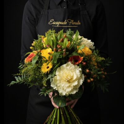 Bouquet "Moisson Champêtre" ​L'Esprit de la Création ​Une composition authentique qui évoque la richesse de la nature. Ce bouquet joue sur des contrastes de formes et de matières, alliant la robustesse du chou d'ornement à la finesse des fleurs champêtres. Avec ses nuances ensoleillées de jaune et d'orange, il apporte une ambiance chaleureuse et rustique, parfaite pour une décoration naturelle ou pour offrir un morceau de jardin. ​Détails de la Composition ​Chaque création est assemblée avec soin pour mettre en valeur les textures : ​Pièce Centrale : Un chou d'ornement (Brassica) majestueux qui donne tout son caractère au bouquet. ​Fleurs de Saison : Un mélange dynamique de Germinis jaunes et oranges pour la luminosité, complété par l'élégance de l'Alstroemeria (Astro Maria) orange. ​Finitions & Textures : Des baies décoratives pour le relief et un feuillage varié sélectionné pour son aspect sauvage et naturel.
