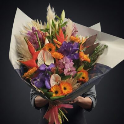 Bouquet "Paradis Tropical" ​L'Esprit de la Création ​Une véritable explosion de couleurs et de formes exotiques qui transporte immédiatement vers des horizons lointains. Ce bouquet "énorme" et spectaculaire est une pièce de design floral conçue pour impressionner par son envergure et sa force visuelle. Alliant des textures graphiques et des teintes vibrantes, il incarne l'opulence de la flore tropicale dans une composition à couper le souffle. ​Détails de la Composition ​Ce bouquet d'exception rassemble les plus belles variétés exotiques pour un rendu unique : ​Fleurs de Prestige : Des orchidées Vanda d'un violet profond, des Heliconias orange vif aux lignes architecturales et des Anthuriums crème à la tenue irréprochable. ​Cœur Solaire : Des germinis orangés éclatants et des lys qui apportent une luminosité chaleureuse au centre de la création. ​Architecture & Volume : L'utilisation de plumeaux de pampa, de feuilles de palmier séchées et de feuillages tropicaux graphiques donne à ce bouquet une hauteur et une envergure monumentales. ​Écrin de Présentation : Un emballage luxueux qui souligne la majesté de cette pièce de collection.