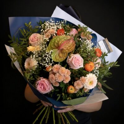 Bouquet "Aurore Boréale" ​L'Esprit de la Création ​Une composition lumineuse et délicate qui évoque la douceur d'un lever de soleil. Ce bouquet se distingue par son harmonie de teintes pastel, mêlant le rose poudré à des notes crème et orangées pour un rendu à la fois chic et apaisant. L’anthurium, avec sa forme graphique, apporte une touche d'exotisme et de modernité à cette création au charme champêtre et raffiné. ​Détails de la Composition ​Chaque bouquet est une pièce unique, assemblée avec soin pour créer un relief texturé : ​Fleurs Majeures : De magnifiques roses roses aux pétales veloutés, accompagnées d'un anthurium majestueux qui devient la pièce maîtresse du bouquet. ​Cœur de Bouquet : Un mélange tendre de germinis et de Santinis aux nuances crème pour une luminosité douce. ​Touches de Saison : Des fleurs de saison aux teintes orangées (renoncules ou oeillets) qui apportent de la chaleur et du dynamisme à l'ensemble. ​Finition Vaporeuse : Un nuage de gypsophile blanc pour la légèreté et le volume. ​Écrin Végétal : Un travail sur le feuillage varié (pistachier, eucalyptus) qui souligne les couleurs et assure une tenue impeccable.